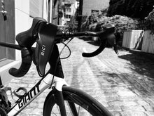 Load image into Gallery viewer, Closeup of a white Giant Roadbike with two Bici Shields attached to it's brake levers. These smooth black plastic hand protectors block wind and keep rider hands warm during winter cycling.